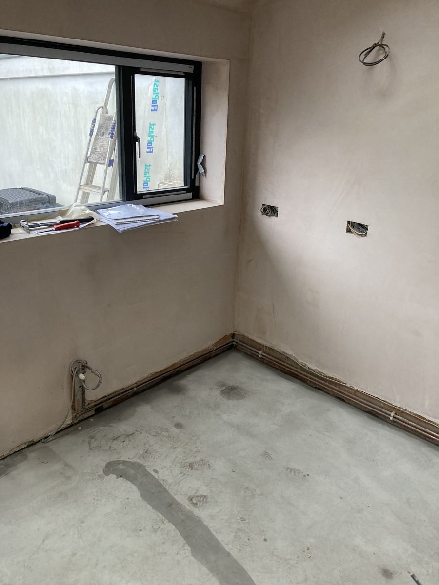 The bare plastered extension before kitchen fitting, first-fix pipework visible