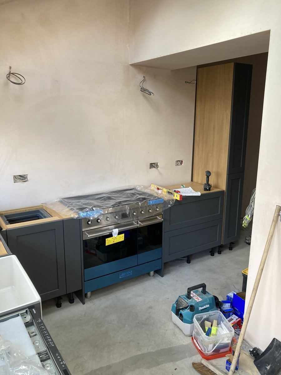 Cabinetry and range cooker being fitted against the bare plaster