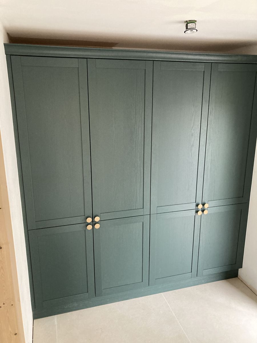 Floor-to-ceiling green shaker cabinetry with brass knobs, doors closed