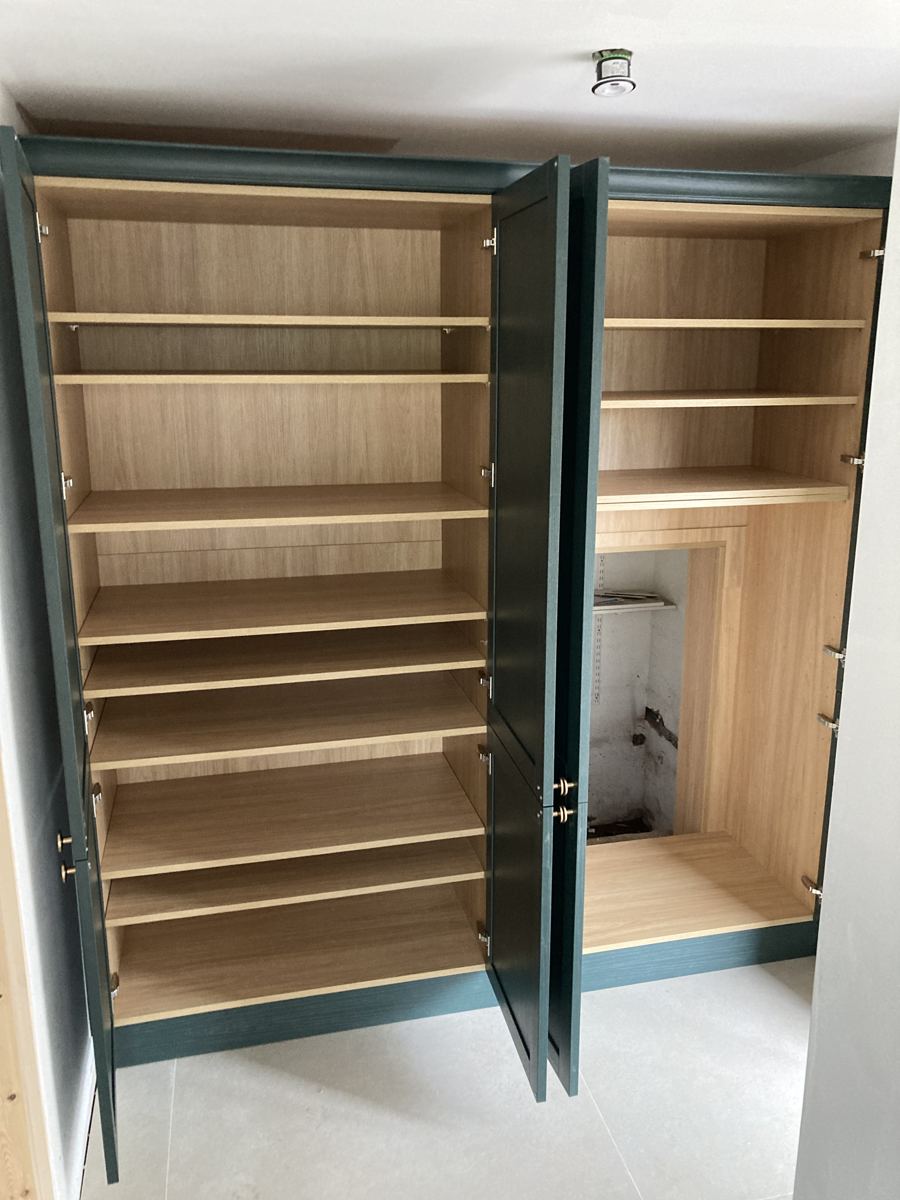 Oak-lined hidden pantry revealed behind green shaker cabinetry