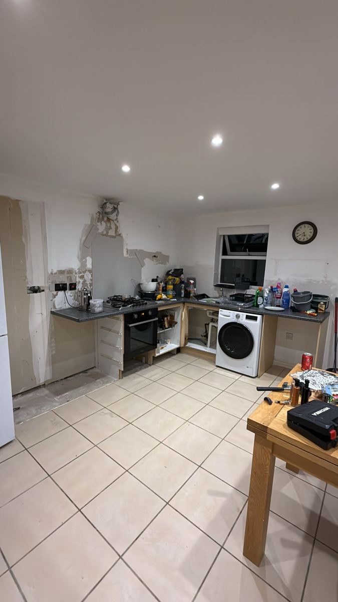 The old kitchen mid strip-out, with dated grey worktops and tiled floor