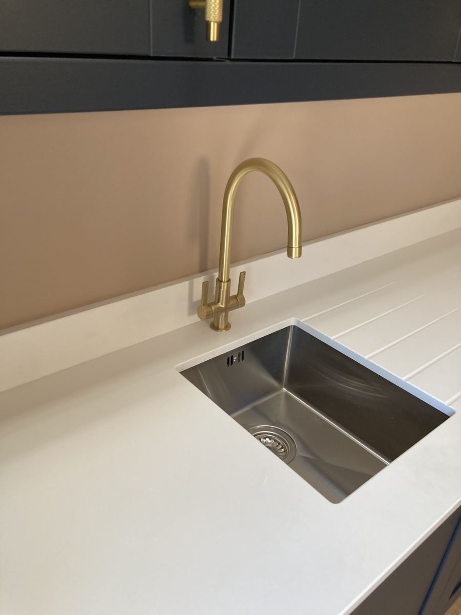 Brushed brass swan-neck tap over undermounted sink with drainer grooves cut into white quartz